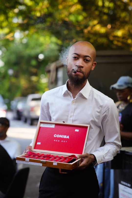 A cigar host presenting a box of Cohiba Red Dot cigars streetside